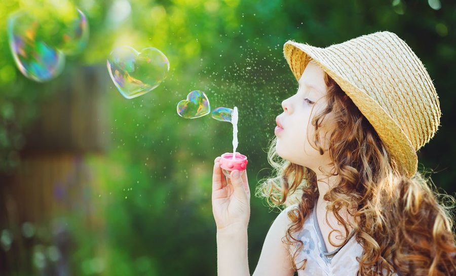 Enfant soufflant des bulles de savon en forme de cœur dans la lumière